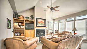 A living room with leather sofas, a fireplace, a ceiling fan, and large windows.