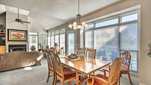 A spacious dining area with a wooden table and chairs, large windows, and a ceiling fan.