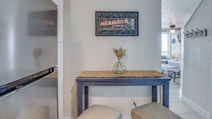 A kitchen with a stainless steel refrigerator, a blue console table with a vase, and two matching stools. - Walk to Shore! Top-floor Daytona Beach Condo (Daytona Beach Shores)