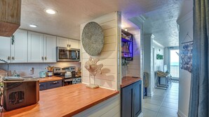 A modern kitchen with white cabinets, a wooden countertop, and a decorative wall piece. - Walk to Shore! Top-floor Daytona Beach Condo (Daytona Beach Shores)
