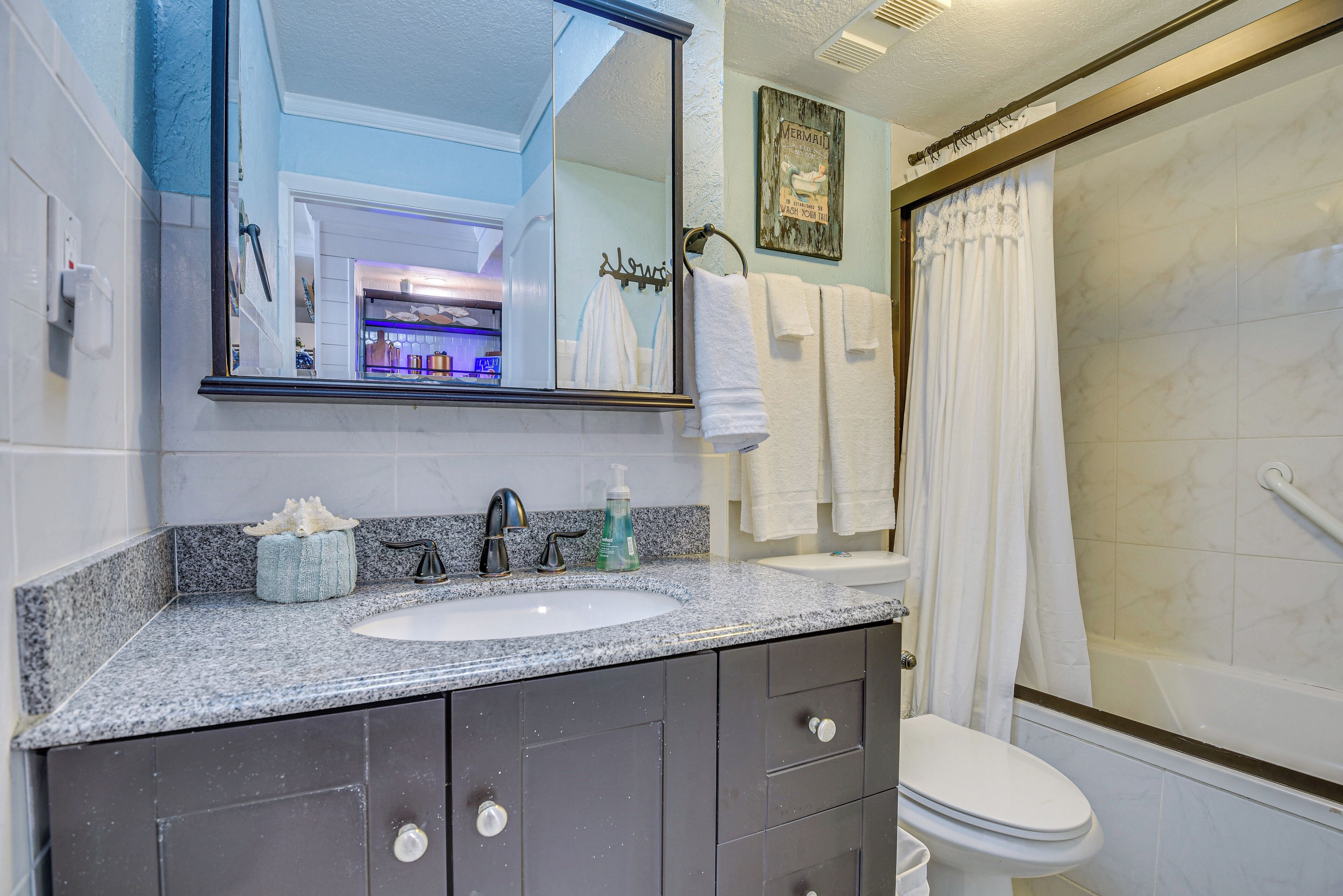 Une salle de bain avec un lavabo blanc, des meubles sombres, un grand miroir et un espace douche.