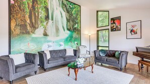 A living room with two grey sofas, a coffee table, a piano, and a large mural of a waterfall. - Pet-friendly Vacation Rental w/ Lake Access (Newton)