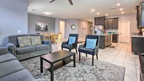 A modern living room with a sofa, armchairs, and a coffee table. A ceiling fan is visible, and the room leads to a kitchen area with cabinets and a refrigerator. - Quiet Family Home w/ Yard ~ 3 Mi to Luke Afb! (Glendale)