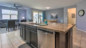 A modern kitchen with a central island, stainless steel appliances, and a dining area with a sofa and chairs. - Quiet Family Home w/ Yard ~ 3 Mi to Luke Afb! (Glendale)