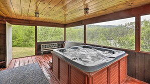 A wooden deck with a hot tub, large windows, and a view of a forested area. - Supreme Family Getaway in the White Mountains! (Rumney)