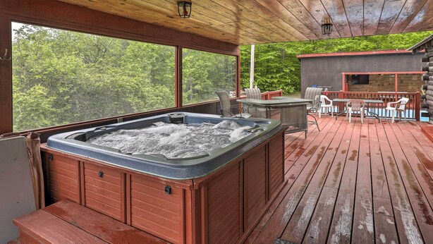 A wooden deck with a hot tub, outdoor seating, and a view of the forest. - Supreme Family Getaway in the White Mountains! (Rumney)