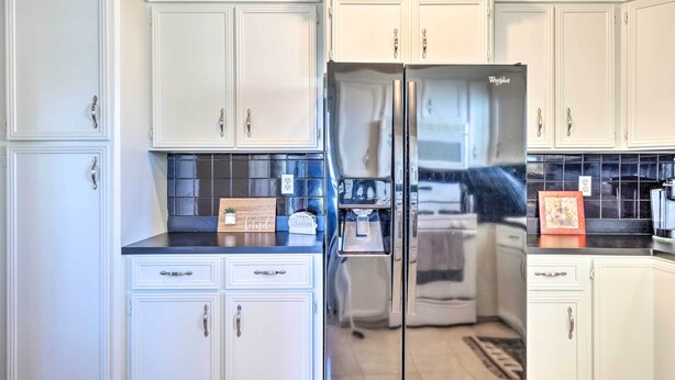 A kitchen with white cabinetry, a stainless steel refrigerator, and a black countertop backsplash. - Pet-friendly Home w/ Patio - 3 Mi to Houston Zoo! (Houston)