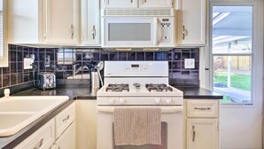 A kitchen with white cabinets, a black countertop, a white stove, and a window with a view of the outside. - Pet-friendly Home w/ Patio - 3 Mi to Houston Zoo! (Houston)