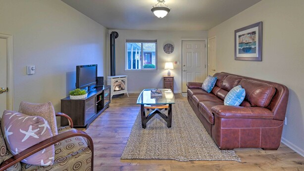 A living room with a brown leather sofa, a glass coffee table, a TV, and a fireplace. - Anacortes Condo - Walk to Town, Marina, + Bay! (Anacortes)
