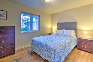 A bedroom with a bed, two bedside tables, a dresser, and a window with a view of a balcony. - Anacortes Condo - Walk to Town, Marina, + Bay! (Anacortes)
