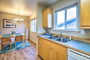 A kitchen with wooden cabinets, a double sink, and a dining area with a table and chairs. - Anacortes Condo - Walk to Town, Marina, + Bay! (Anacortes)