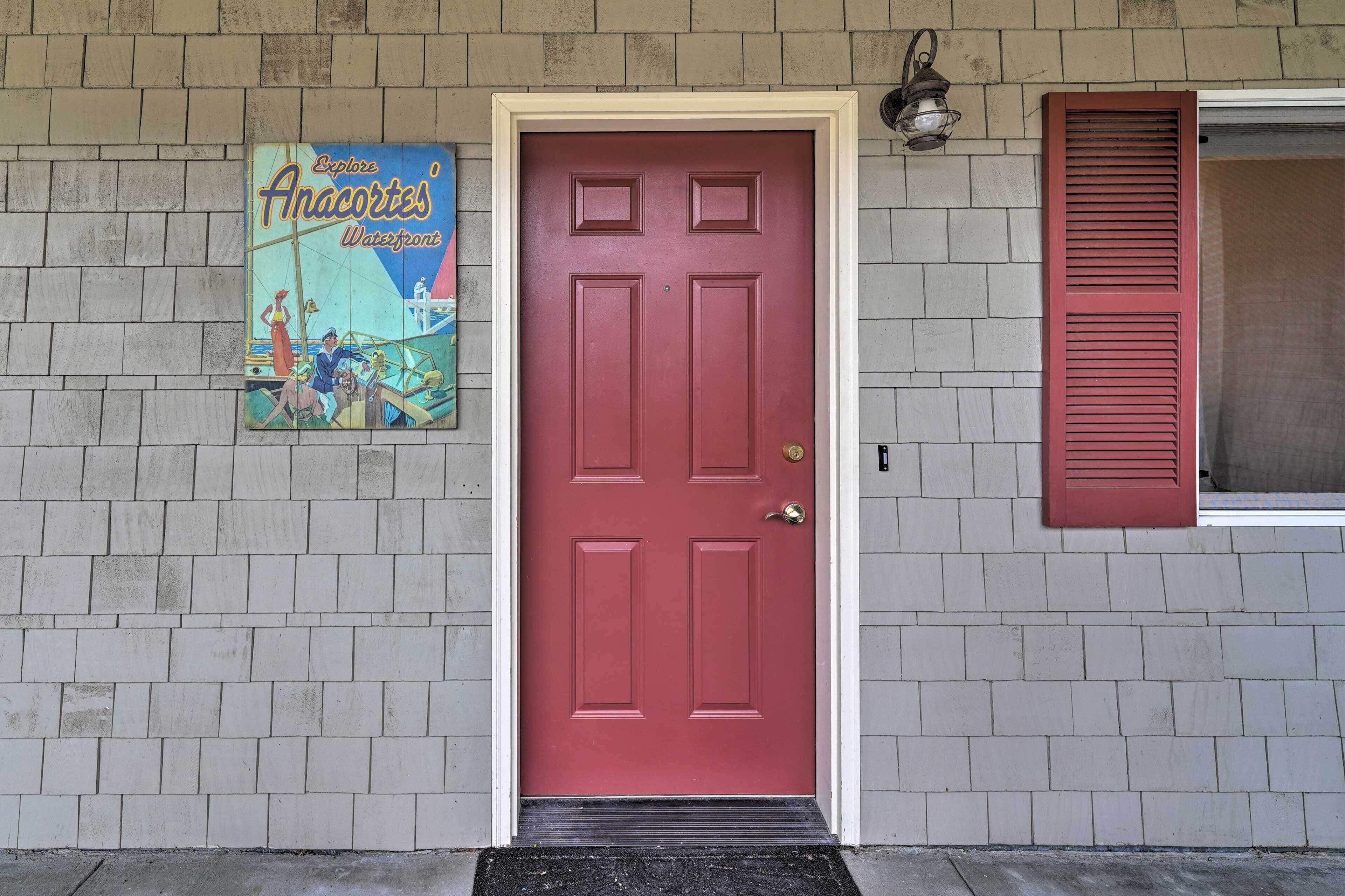 A red door with a white frame, a small step leading up to it, and a poster of a boat on the wall to the left.