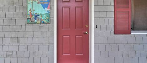 A red door with a white frame, a small step leading up to it, and a poster of a boat on the wall to the left.