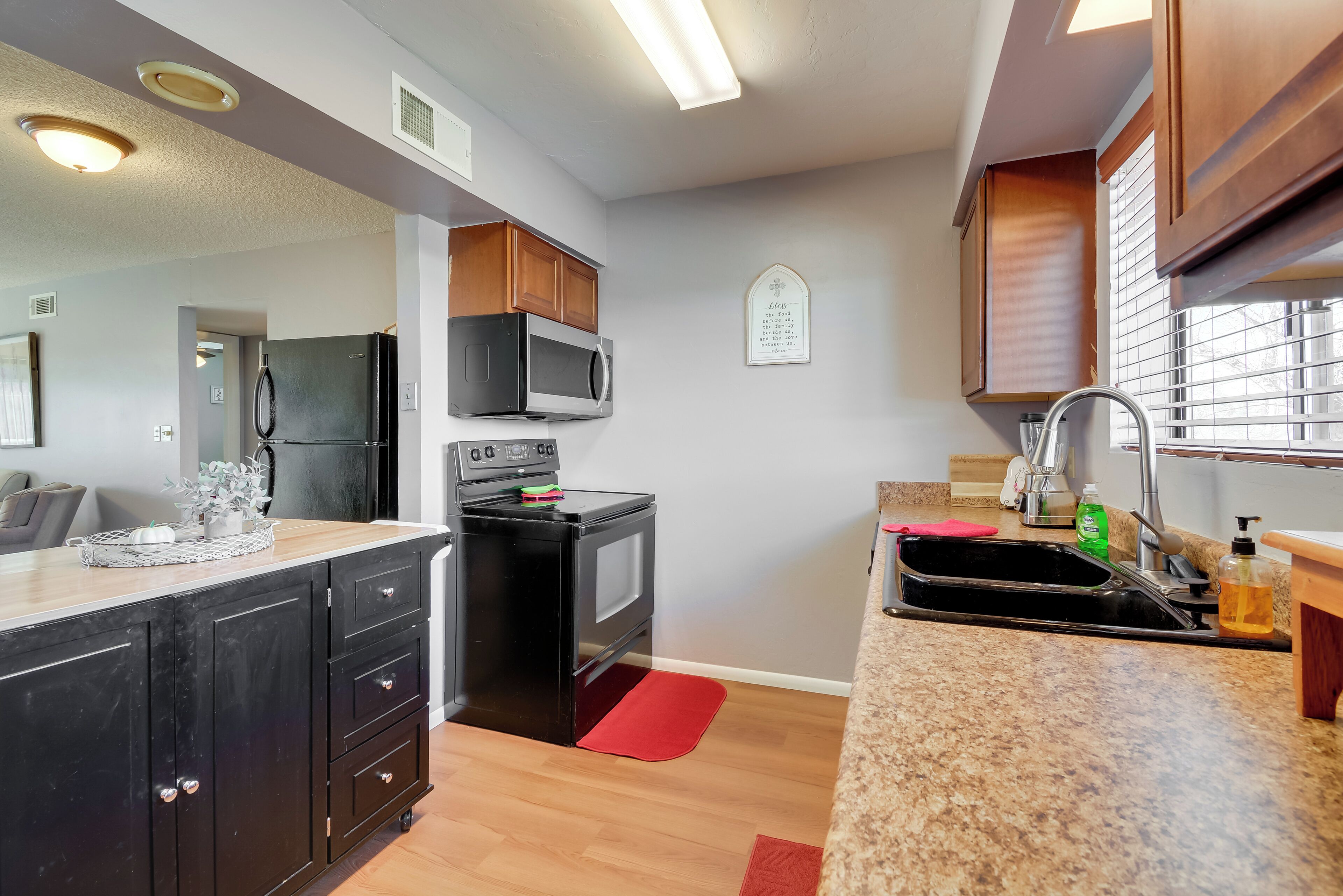 Une cuisine moderne avec un réfrigérateur noir, un four à micro-ondes et une cuisinière. Un tapis rouge recouvre le sol, et des armoires en bois sont placées au-dessus du plan de travail.