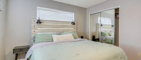 A bedroom with a bed, a nightstand, a ceiling fan, a window with blinds, and a closet with a mirror.