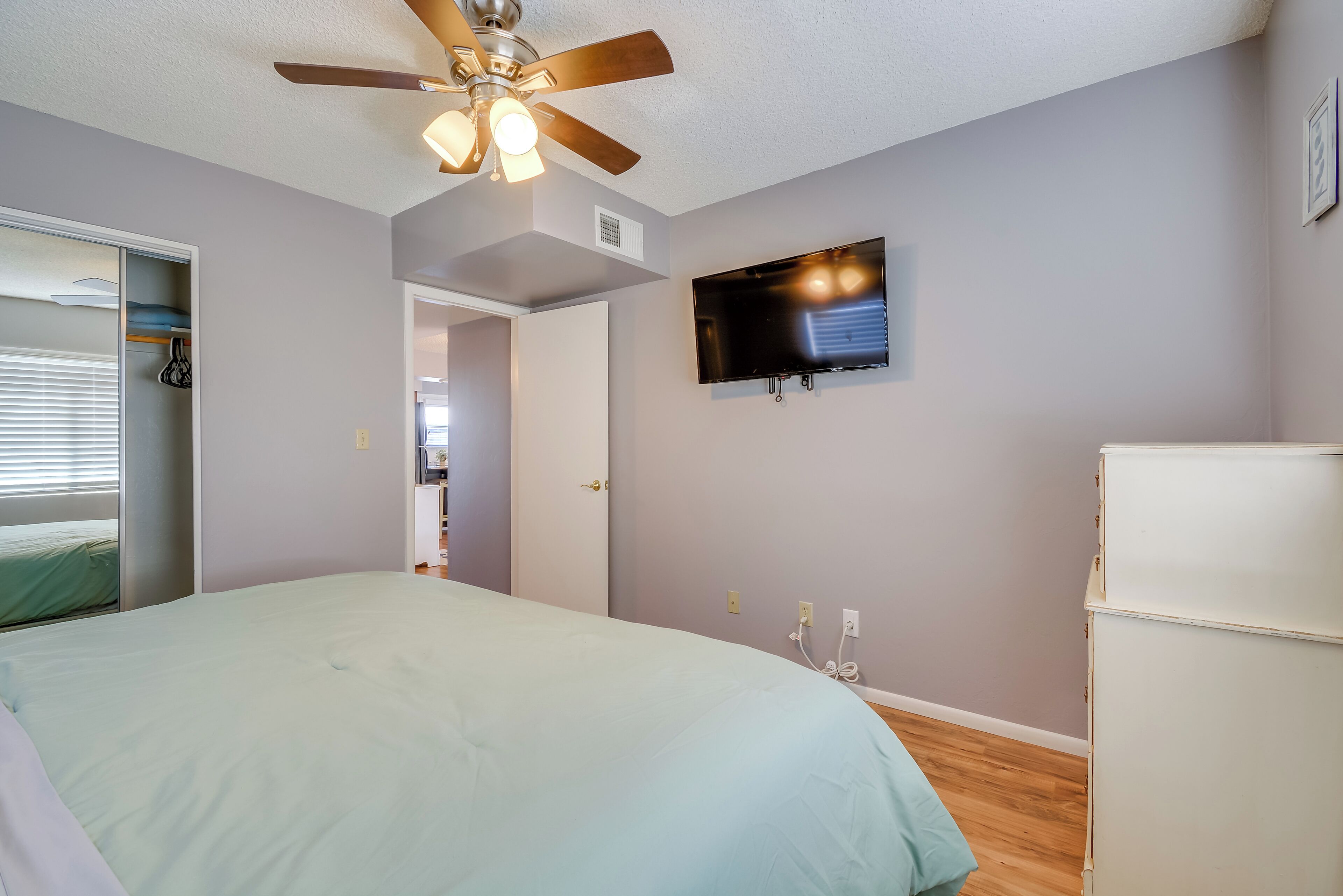 A bedroom with a bed, ceiling fan, TV, and a white dresser.