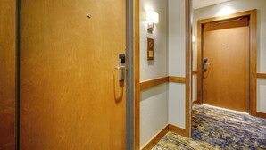 Ein Hotelgang mit Holztüren, einer strukturierten Wand und einem gemusterten Teppich.