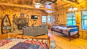 A cozy cabin interior with a bed, a couch, a fireplace, and a large fish mounted on the ceiling. - Mountian View Retreat < 2 Mi to White River! (Mountain View)