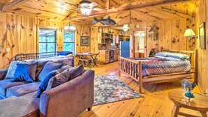 A cozy cabin interior with a wooden ceiling, a bed with a patterned blanket, a sofa with cushions, a dining table, and a kitchen area. - Mountian View Retreat < 2 Mi to White River! (Mountain View)