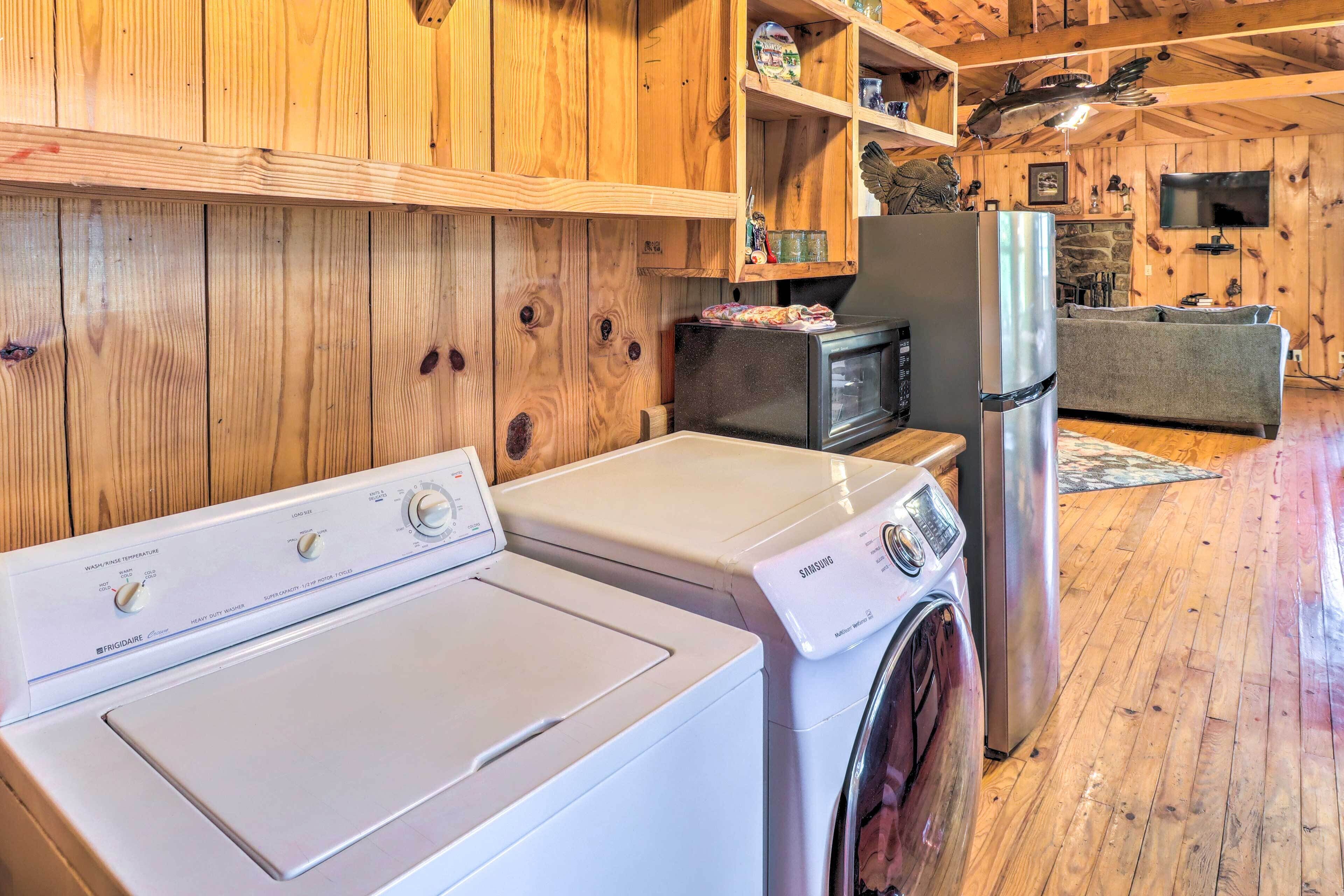 A laundry area with a front-loading washer and dryer, wooden walls, a microwave, and a refrigerator.