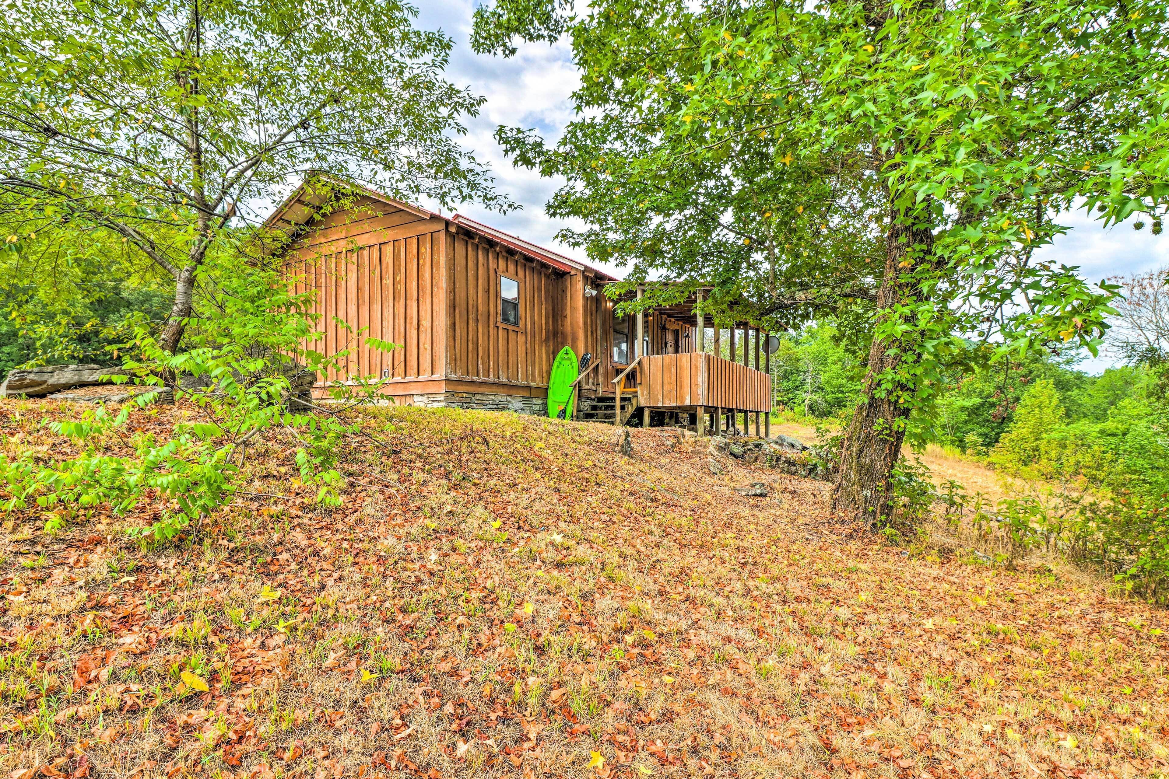 Een houten hut met een veranda, omringd door bomen en een grasheuvel.