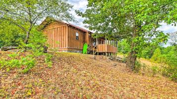 Een houten hut met een veranda, omringd door bomen en een grasheuvel.