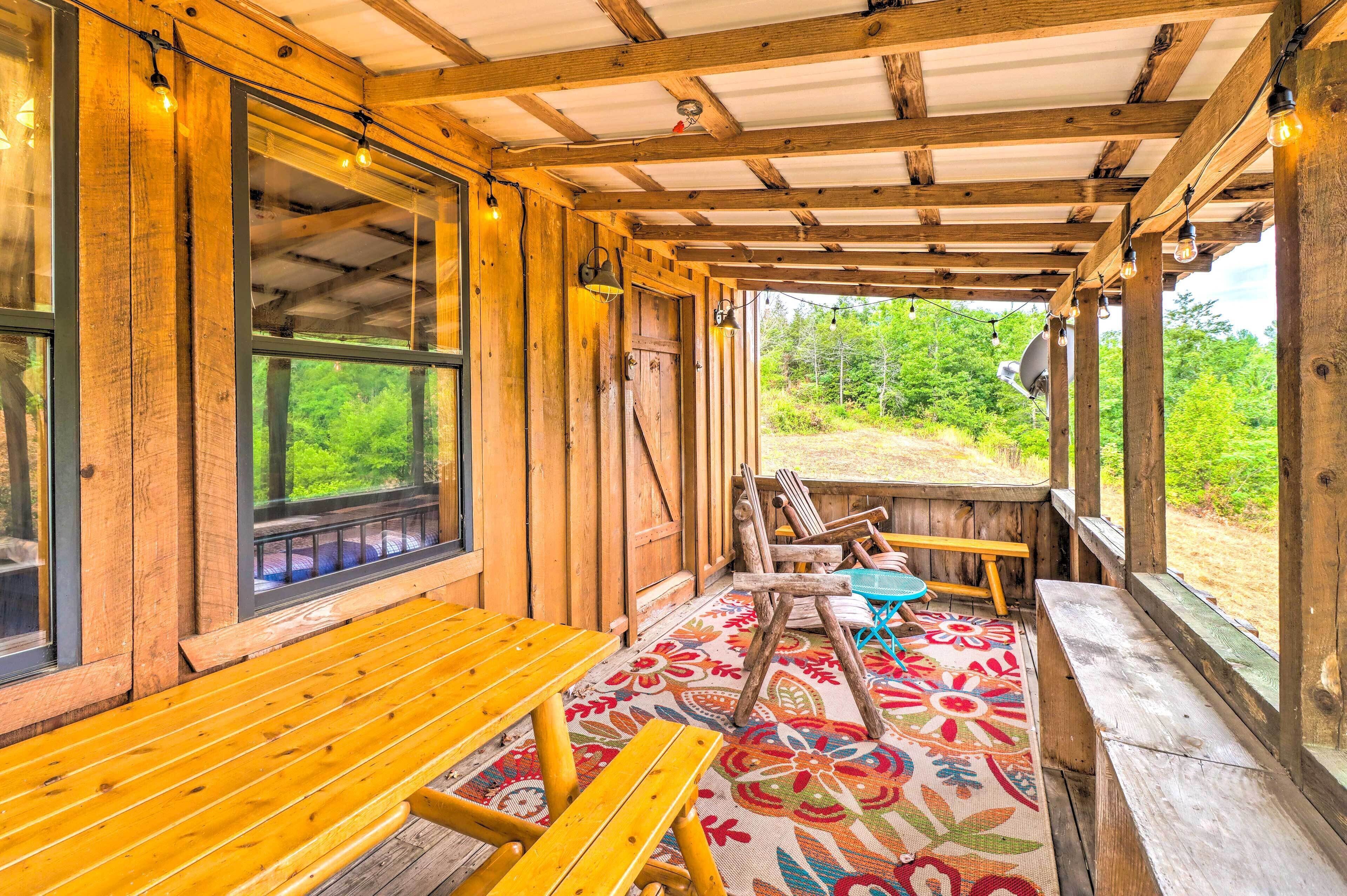 A wooden porch with benches and a colorful rug, overlooking a natural landscape.