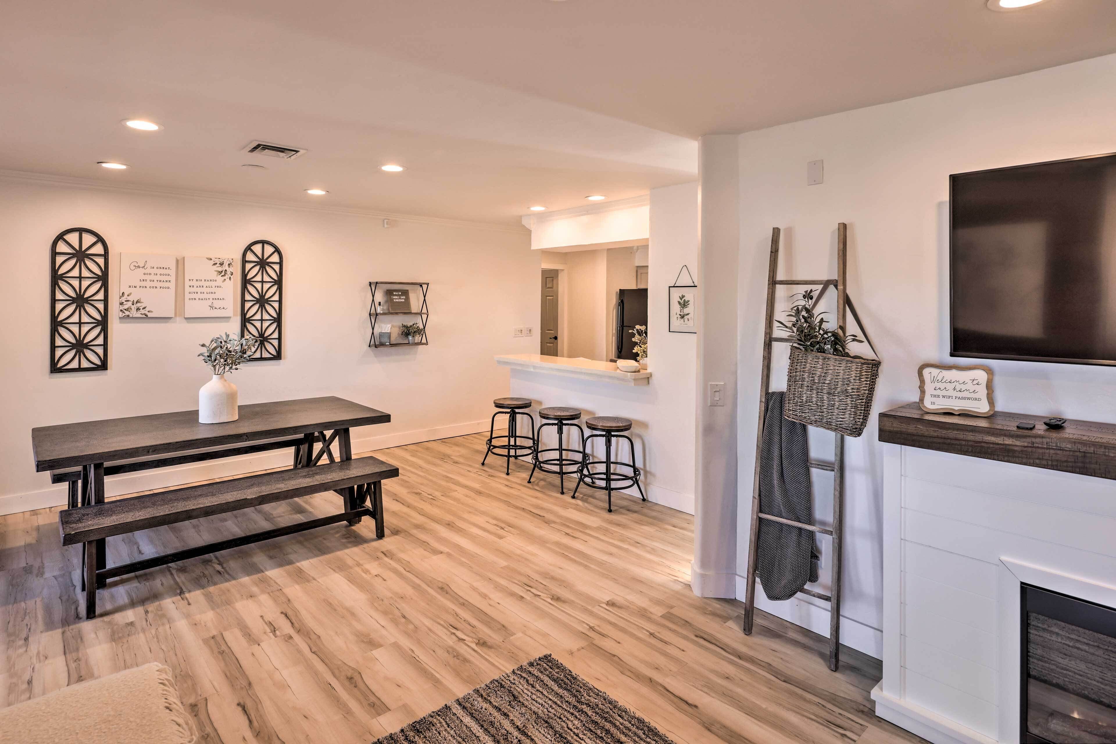 Cozinha moderna com piso de madeira, mesa de jantar com bancos, banquetas, televisão e decoração na parede.