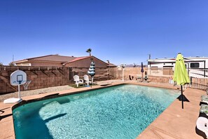 A backyard with a swimming pool, a basketball hoop, and a fenced area with chairs and umbrellas. - Private Pool & Patio: Lake Havasu Home (Lake Havasu City)