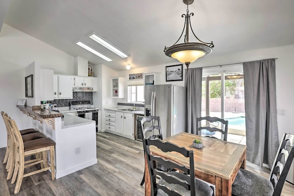 A modern kitchen with white cabinets, a central island, and a dining area with a wooden table and chairs. - 5 Mi to the River! Bullhead City Home w/ Pool (Bullhead City)