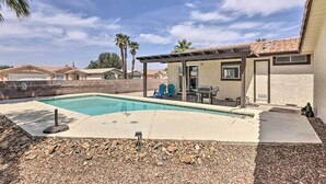 A backyard with a swimming pool, patio furniture, and a covered seating area.