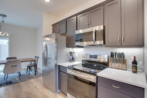 A modern kitchen with stainless steel appliances, a dining area with a wooden table and chairs, and a view of the outdoors. - Modern Townhome ~ 3 Mi to Dtwn Grand Junction (Grand Junction)