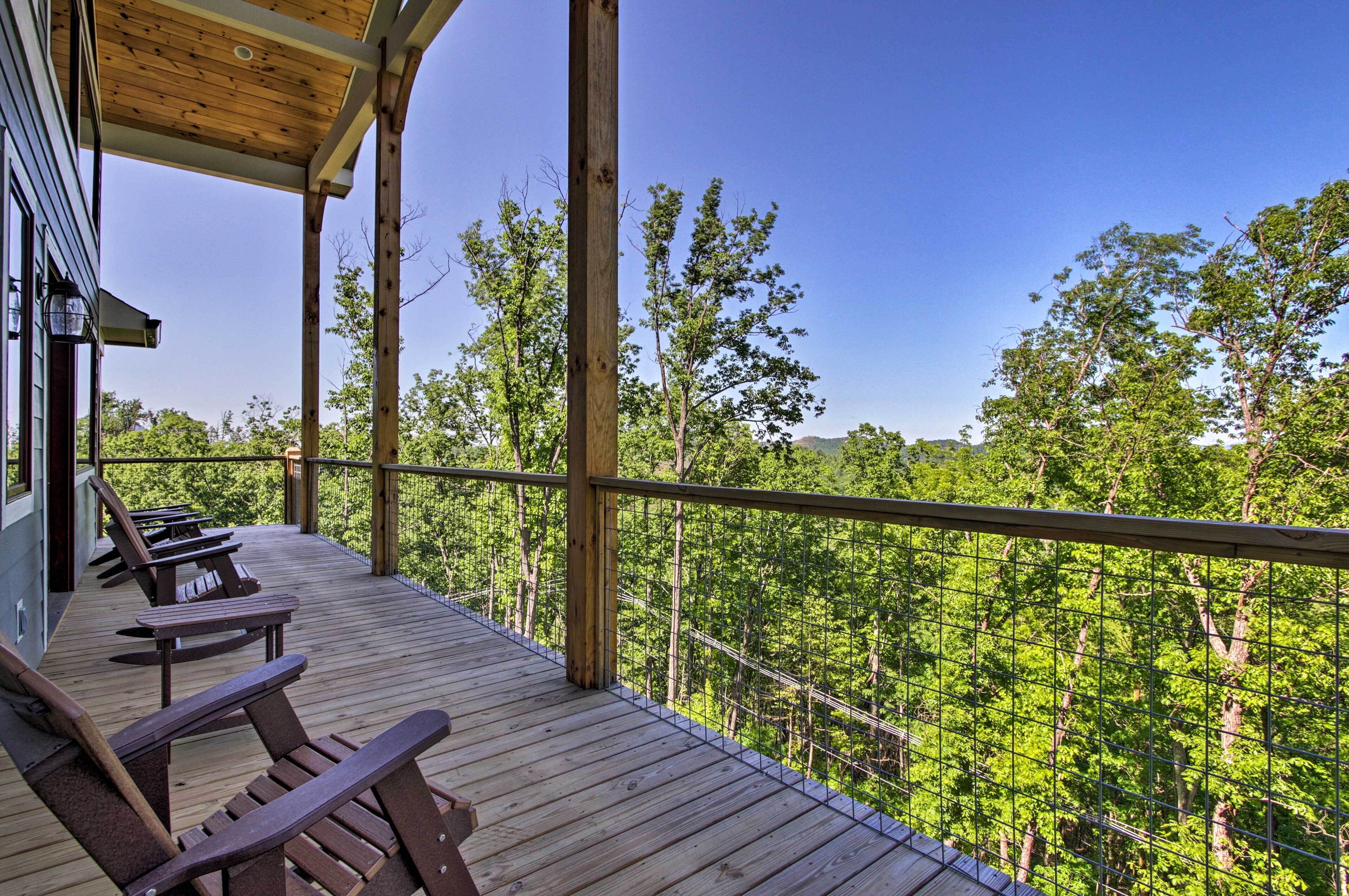 Una terraza de madera con mesas de picnic y vista a un bosque.