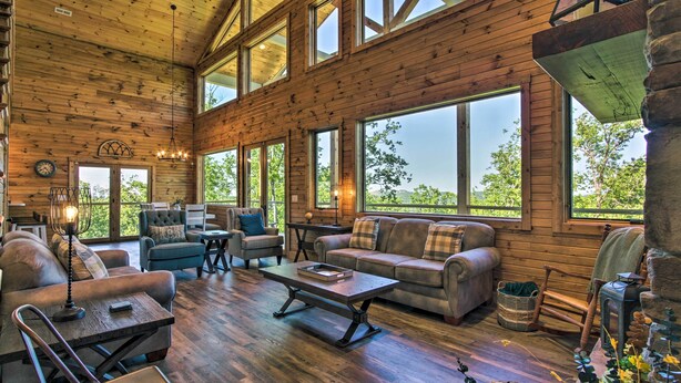 A spacious room with wooden walls and large windows, furnished with sofas, a coffee table, and a dining table.