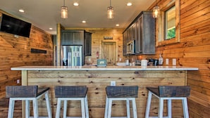 A kitchen with wooden walls, a central island with bar stools, stainless steel appliances, and pendant lighting.