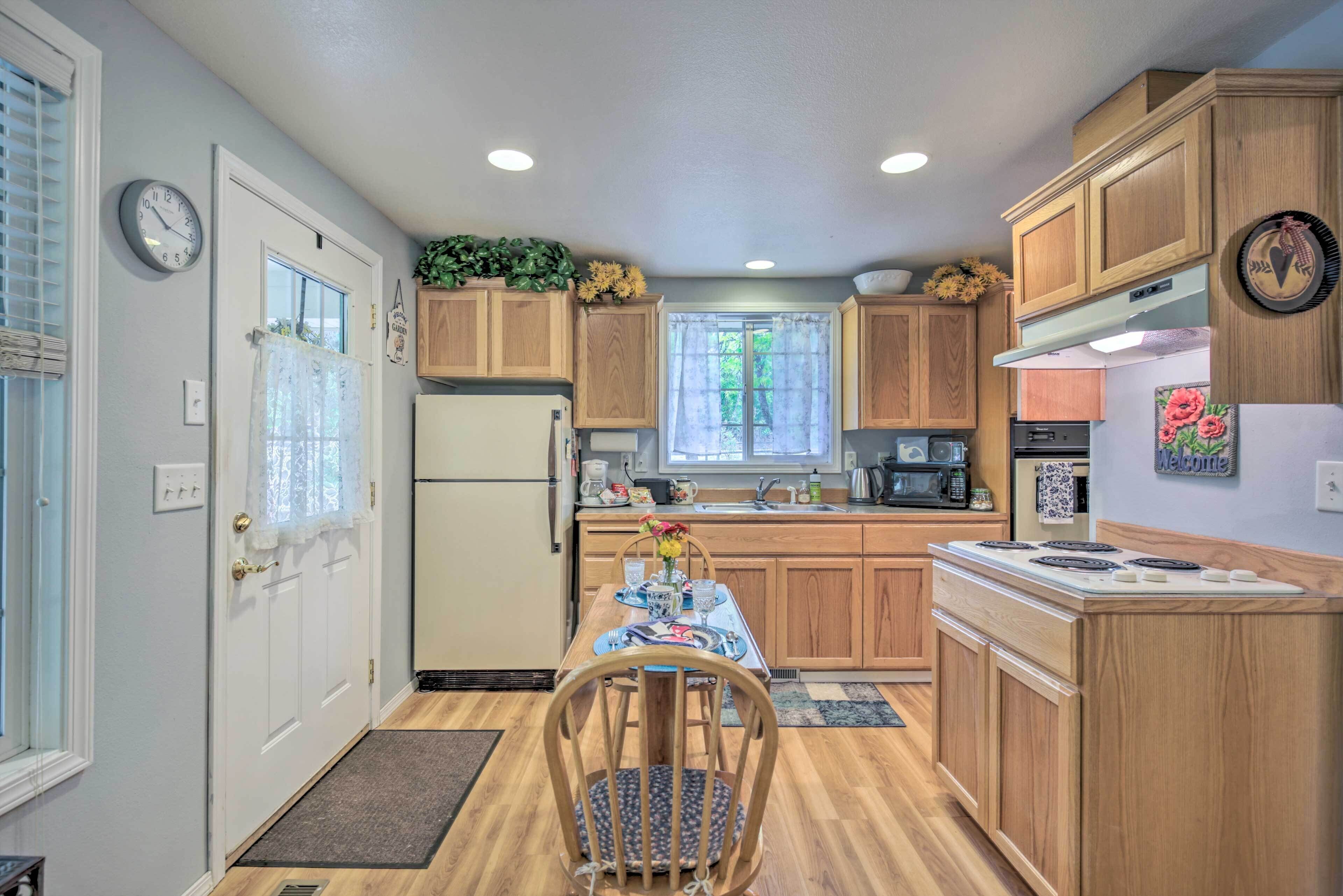 A compact kitchen with wooden cabinets, a refrigerator, a stove, and a dining table with chairs.
