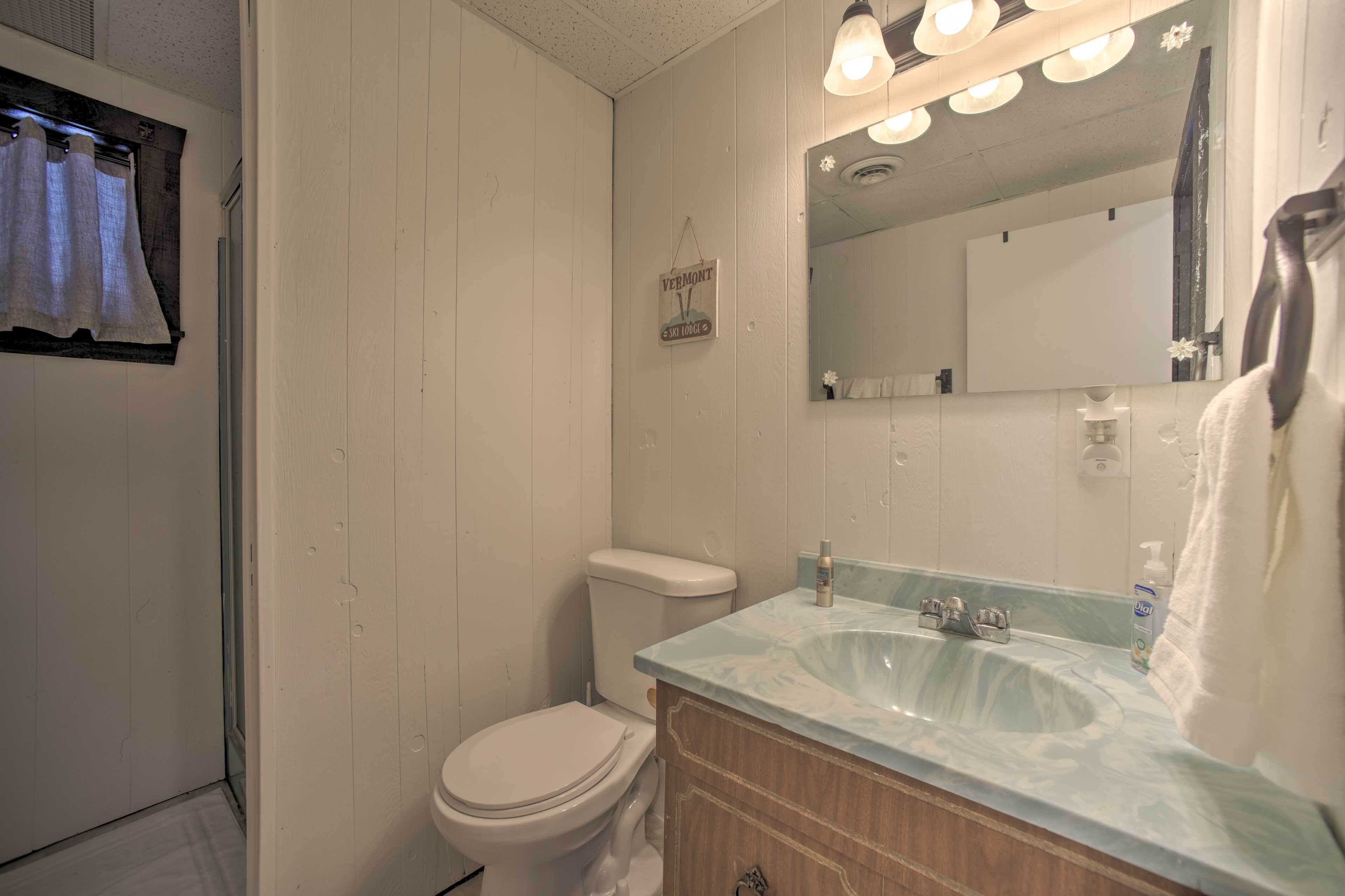 Une salle de bain avec des toilettes blanches, un lavabo doté d’un plan de travail en marbre et un miroir au-dessus du lavabo.