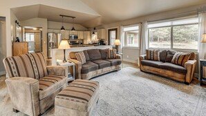 A spacious living room with a large sofa, a smaller sofa, and a loveseat, all arranged around a central rug. There is a kitchen area visible in the background with modern appliances and pendant lighting. - Kalispell Main House < 15 Mi to Flathead Lake (Kalispell)