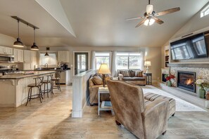 A spacious living area with a fireplace, a large TV, and a kitchen with bar stools. - Kalispell Main House < 15 Mi to Flathead Lake (Kalispell)