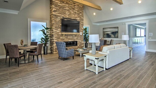 A spacious living room with a stone fireplace, a flat-screen TV mounted on the wall, a dining area with a round table and chairs, and a large sofa.