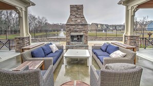 An outdoor patio with wicker furniture, a stone fireplace, and a view of houses in the background.