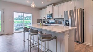 A modern kitchen with a large island, stainless steel appliances, and pendant lighting.