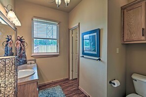 A bathroom with a wooden vanity, a sink, a toilet, and a window with blinds. - Charming Vian Retreat w/ Private Deck & Grills! (Vian)