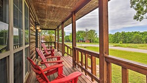 Una terraza de madera con sillas Adirondack rojas, un espacio cubierto con techo de madera y vistas a una carretera y follaje.
