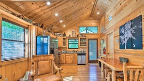 A wooden cabin interior with a dining area, kitchen, and large windows. - Broken Bow Hideaway w/ Hot Tub & Fire Pit! (Broken Bow)