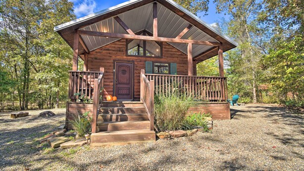 A rustic cabin with a wooden exterior, a porch, and a gravel driveway surrounded by trees. - Broken Bow Hideaway w/ Hot Tub & Fire Pit! (Broken Bow)
