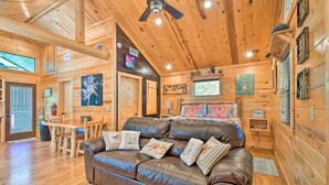 A cozy cabin interior with a wooden floor, a leather couch, a dining table, and a ceiling fan. - Broken Bow Hideaway w/ Hot Tub & Fire Pit! (Broken Bow)