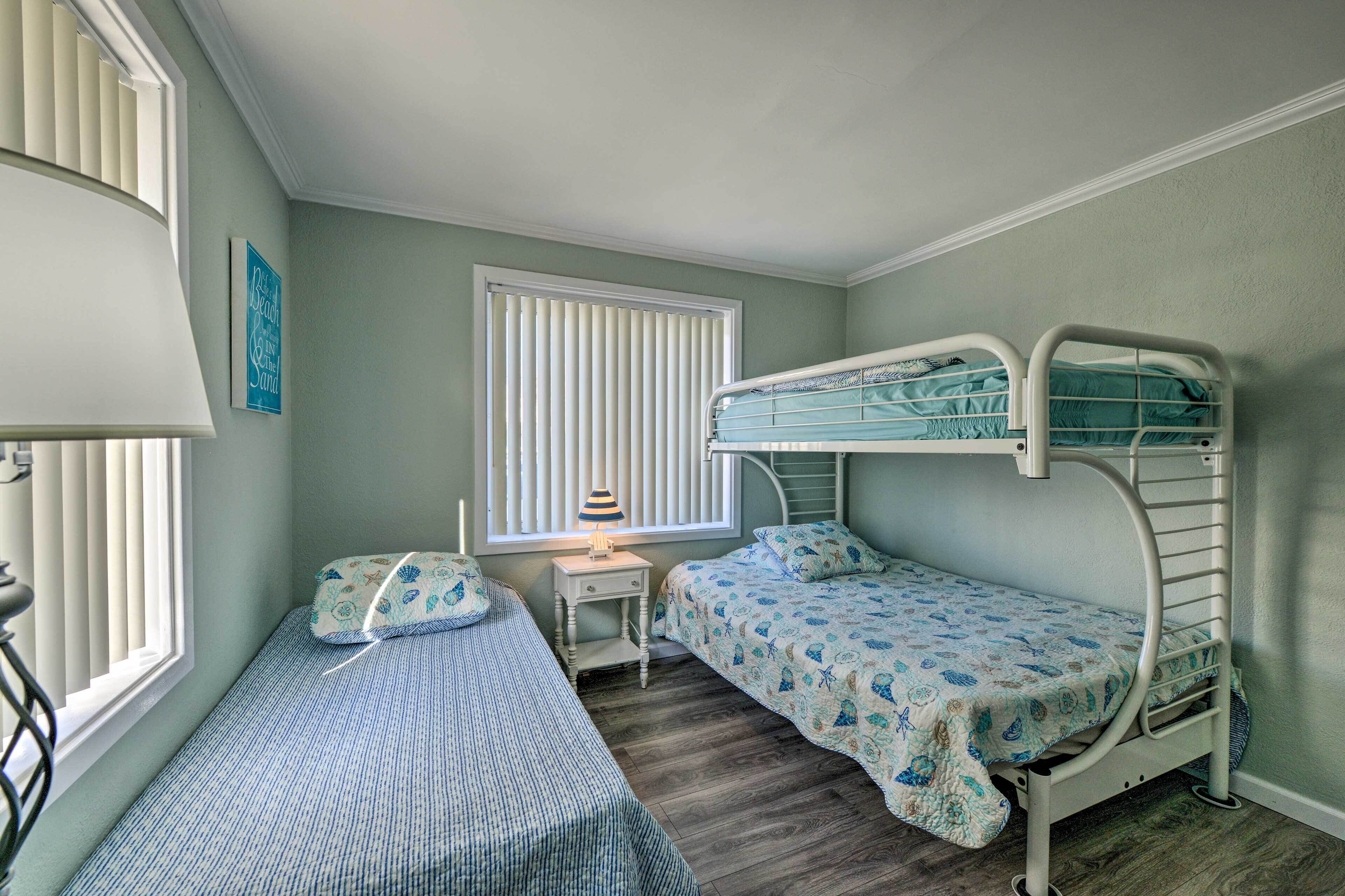 Un dormitorio con dos camas individuales, una ventana con persianas, una mesita de noche con lámpara y una cama nido.