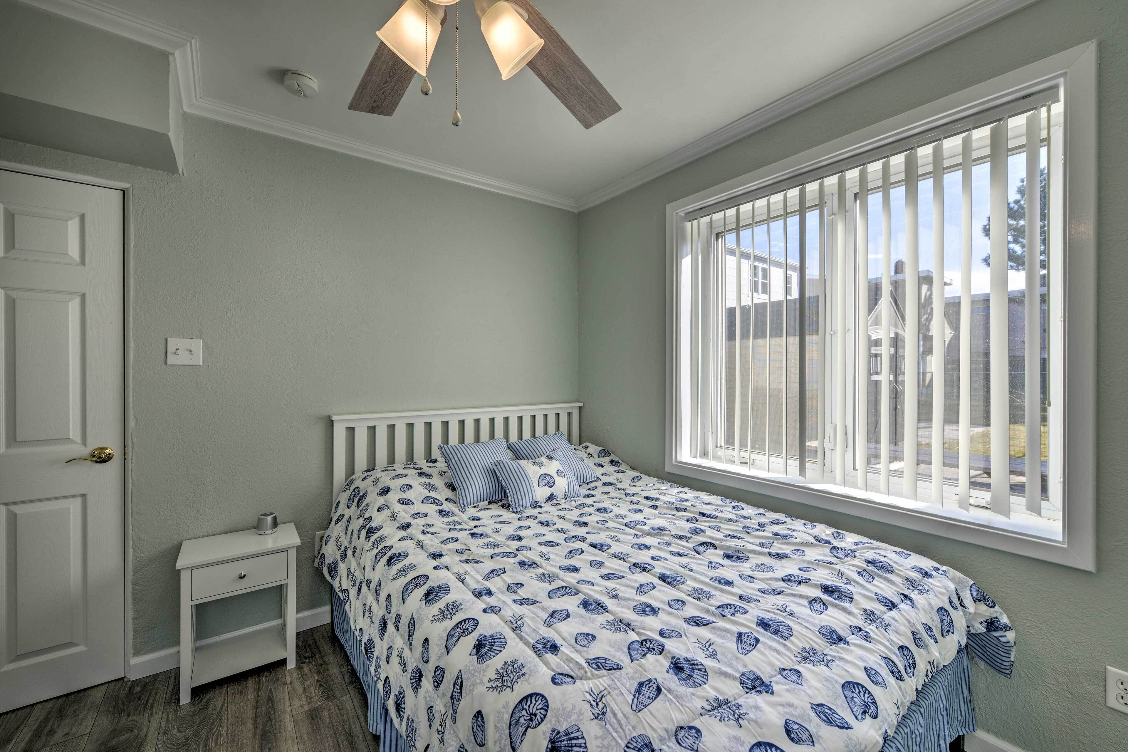 Une chambre à coucher avec un lit, une table de chevet, une fenêtre avec des stores et un ventilateur de plafond.