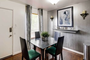 A dining area with a table, chairs, a potted plant, and a framed artwork on the wall.